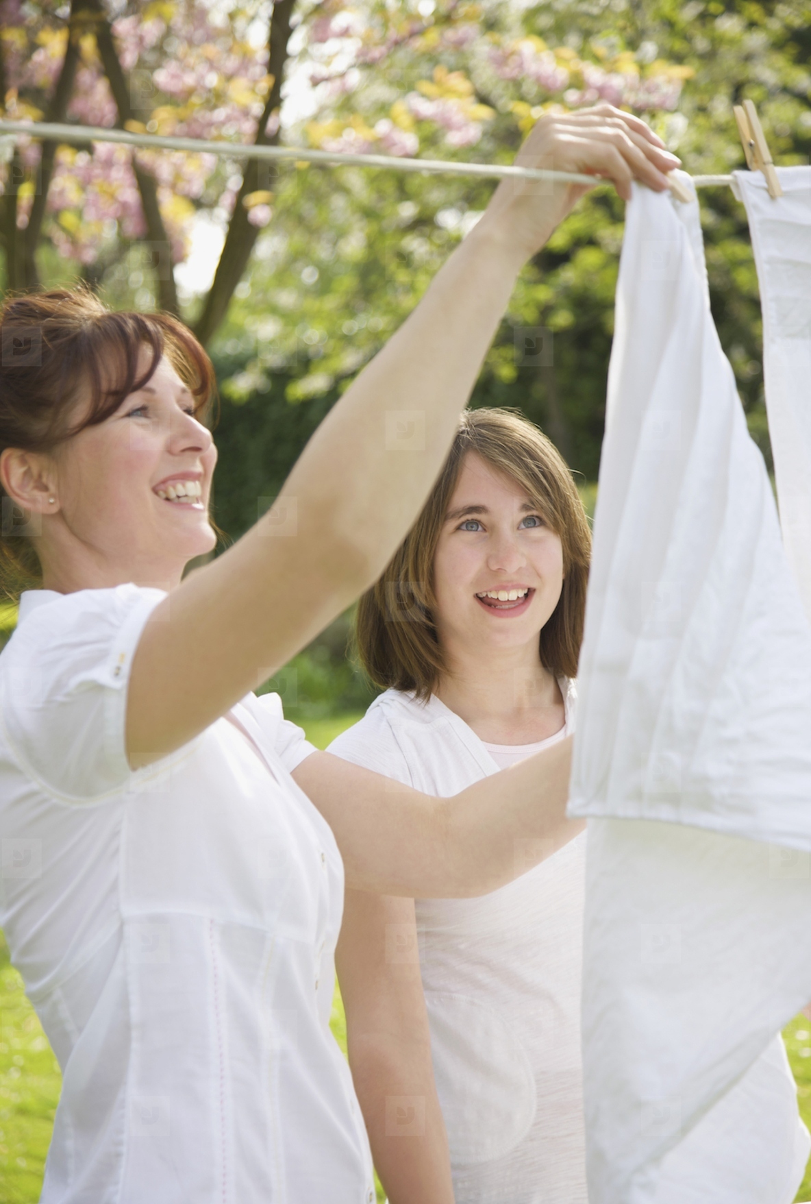Smiling woman and teenage girl hanging linens on a clothesline