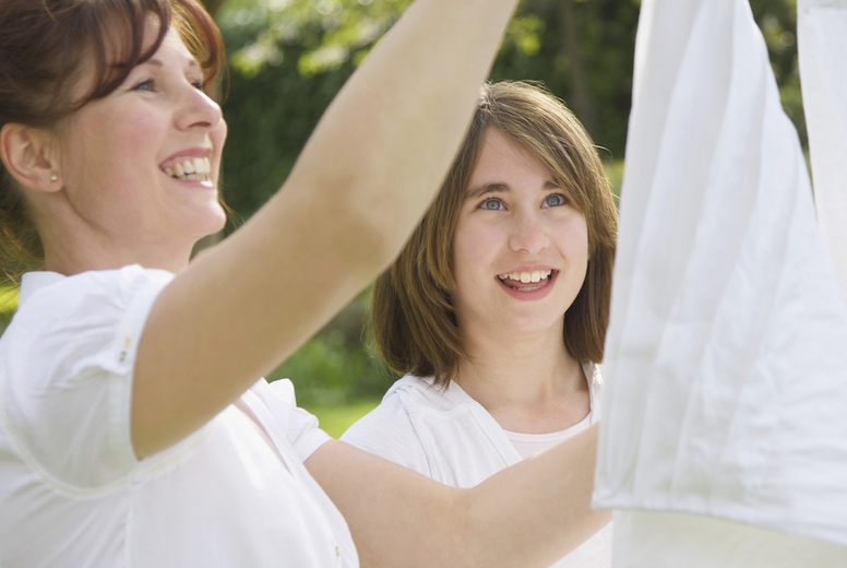 Smiling woman and teenage girl hanging linens on a clothesline