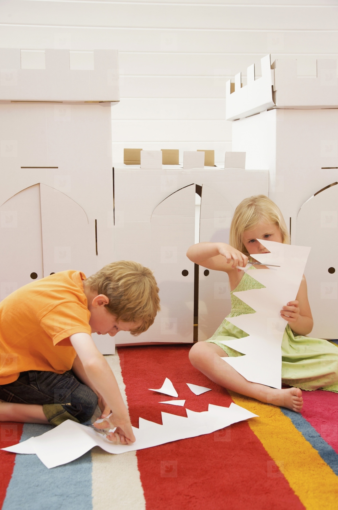 Boy and girl sitting in front of a cardboard castle cutting paper