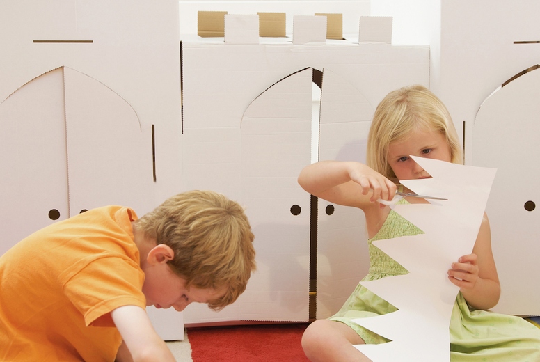 Boy and girl sitting in front of a cardboard castle cutting paper