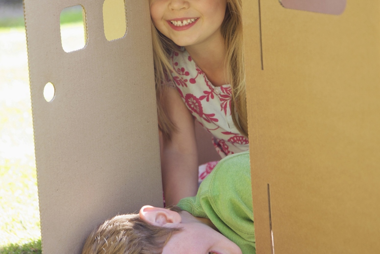 Boy and girl smiling in the doorway of a cardboard playhouse