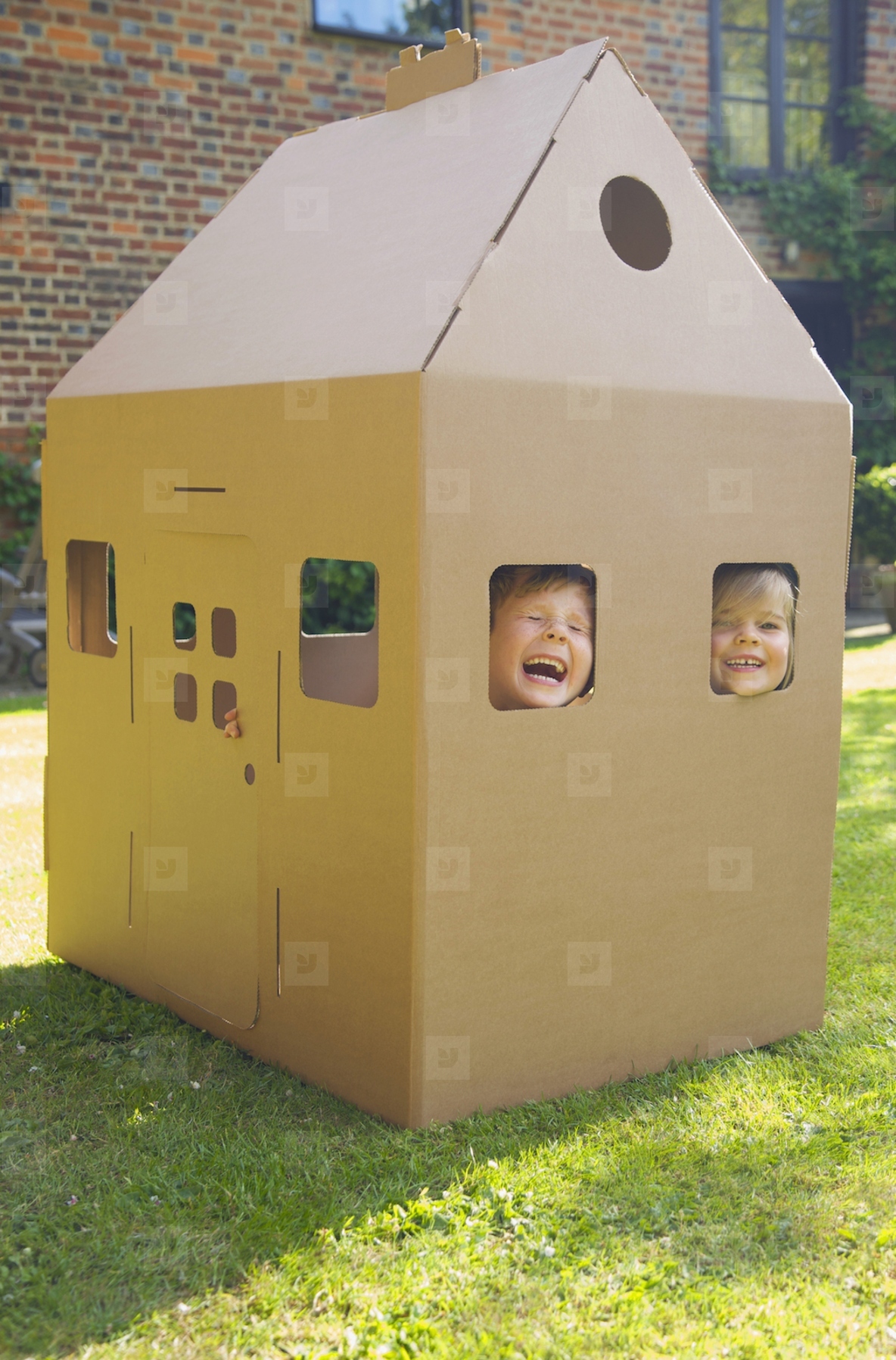 Boy and girl looking out from the windows of a cardboard playhouse laughing and screaming