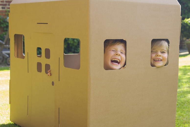 Boy and girl looking out from the windows of a cardboard playhouse laughing and screaming