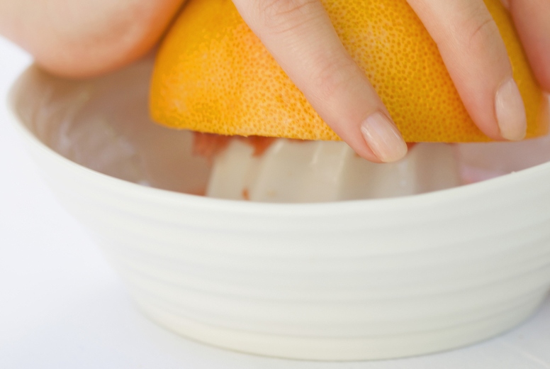 Close up of a womans hand squeezing an orange on a juicer