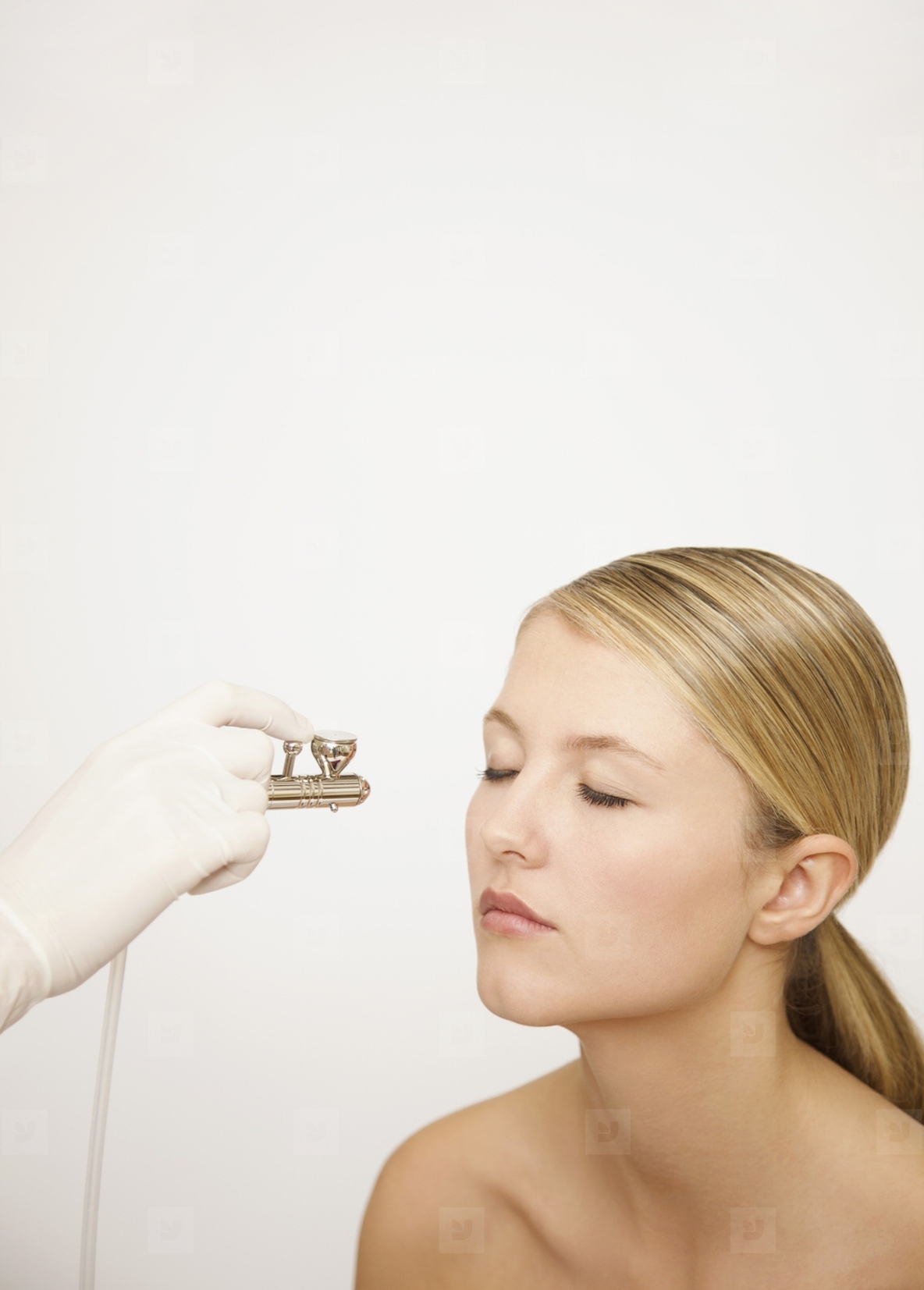 Beauticians hand applying make up with an airbrush to a womans face