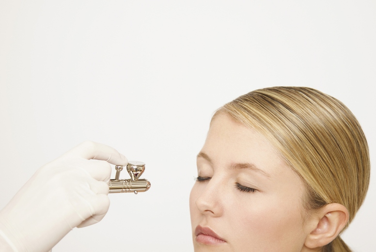 Beauticians hand applying make up with an airbrush to a womans face