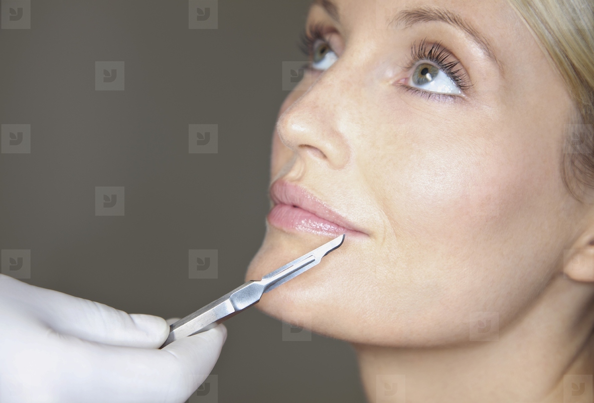 Doctors Hand Holding Surgical Scalpel in front of Womans Face
