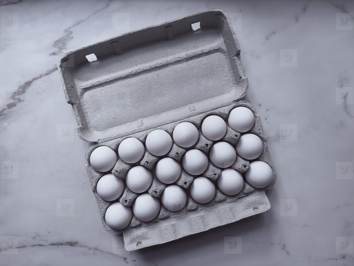 View from above 18 white eggs in egg carton on marble surface