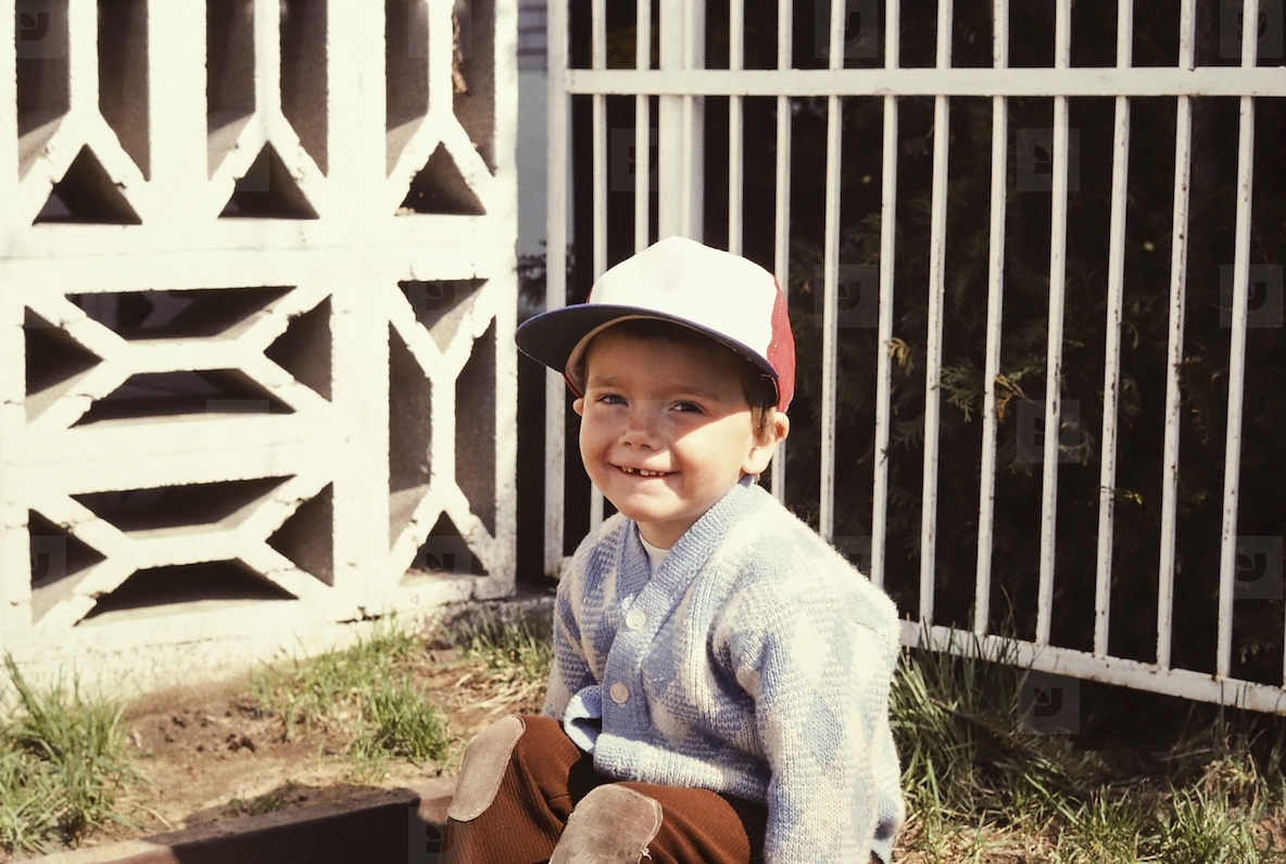 Portrait cute preschool in baseball cap sitting in sunny yard