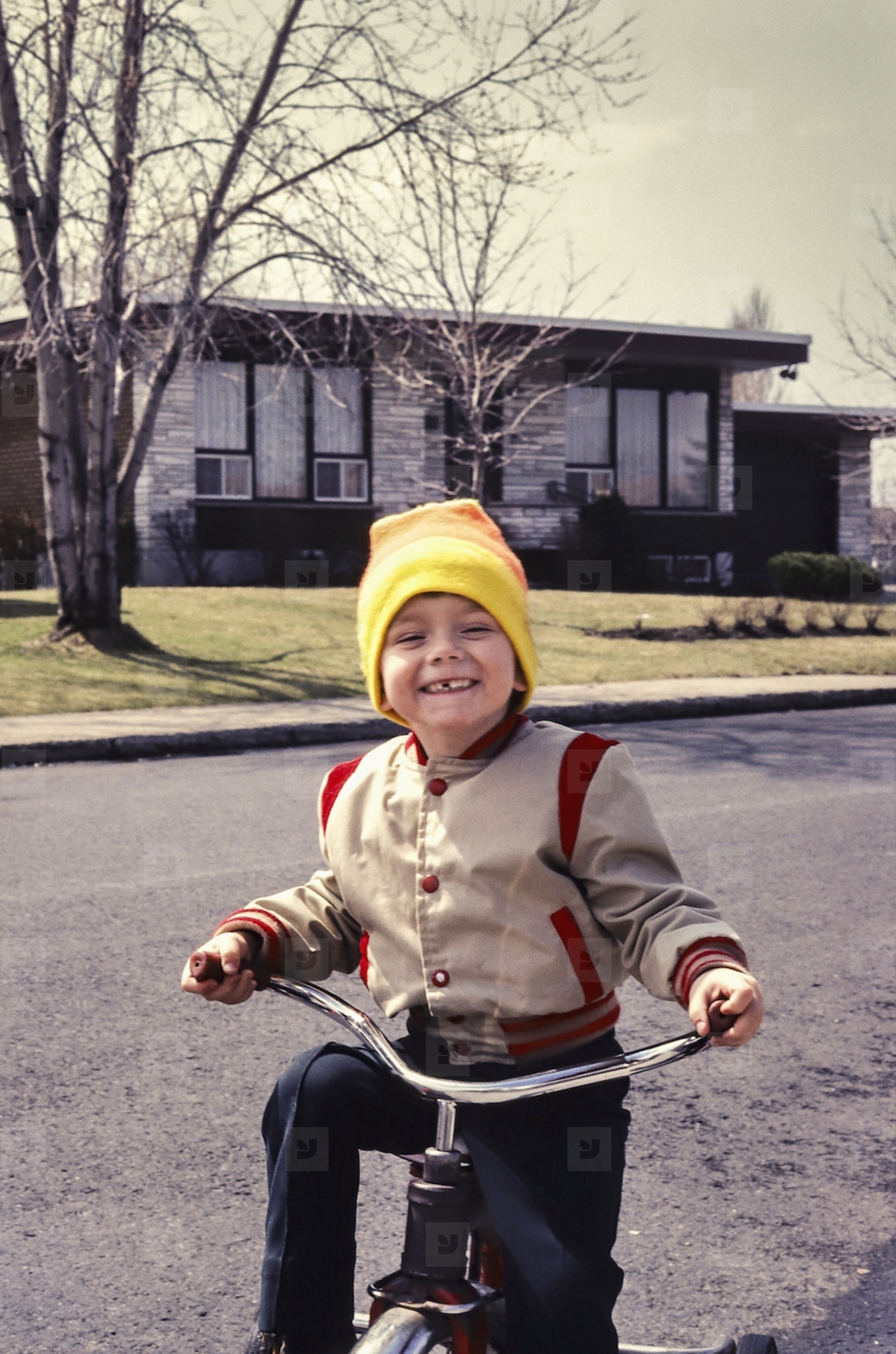 Portrait cute boy in stocking cap riding tricycle in sunny street outside house