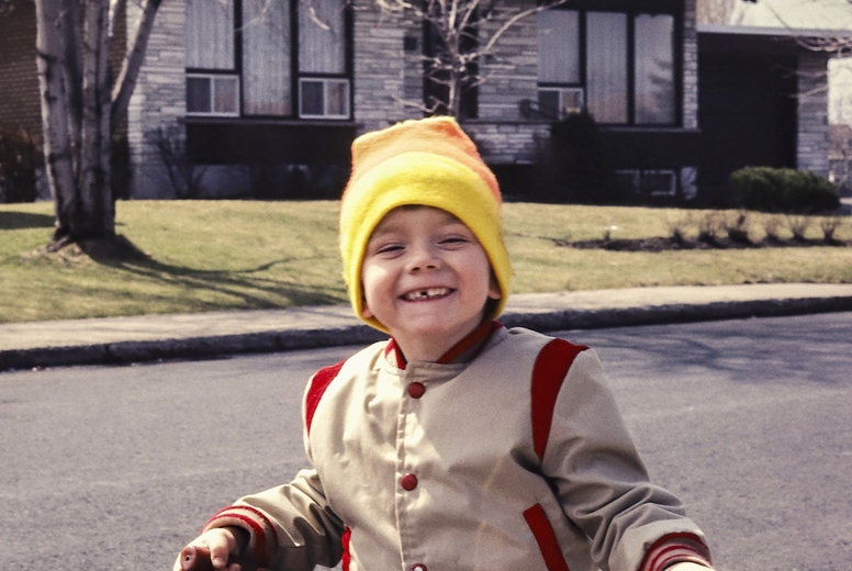 Portrait cute boy in stocking cap riding tricycle in sunny street outside house