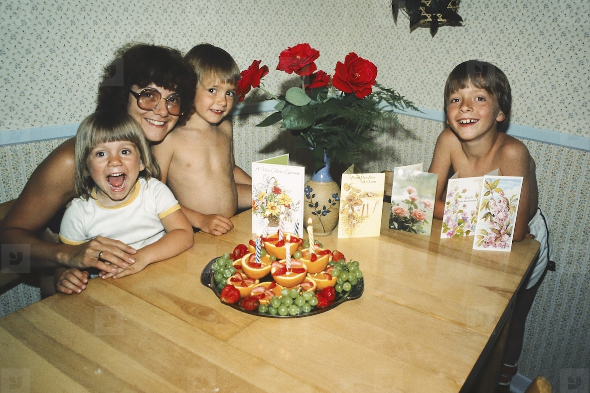 Portrait happy mother and children celebrating birthday with fruit and cards at dining table