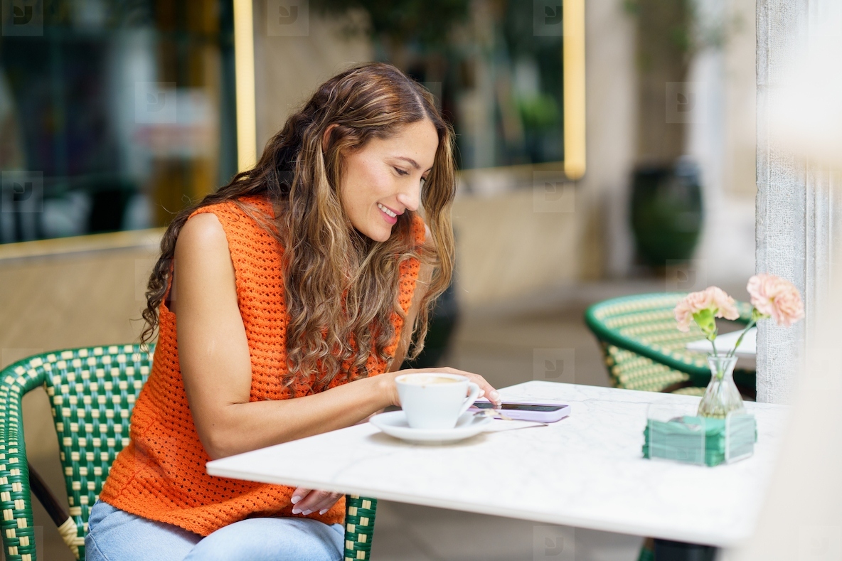 Woman using phone sitting on the terrace of a cafeteria