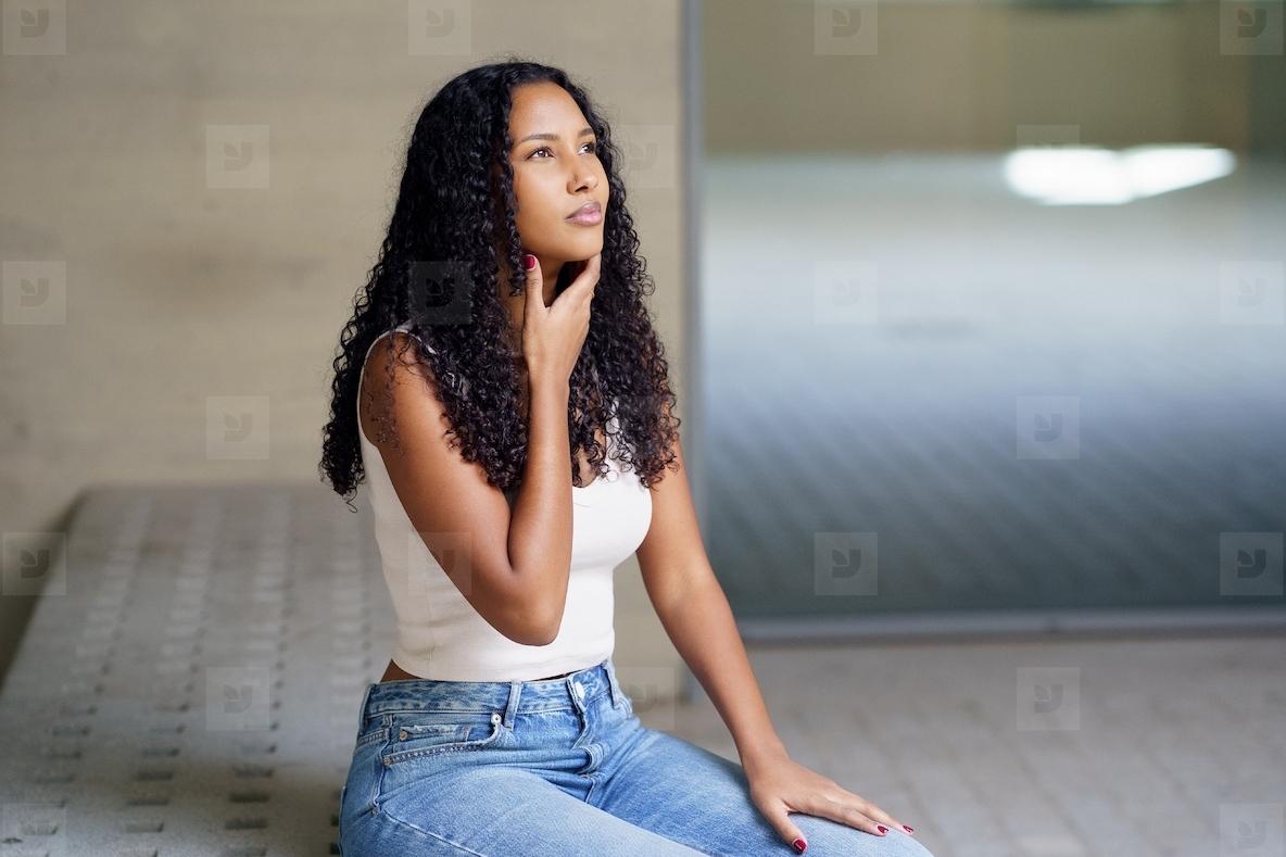 A Thoughtful Young Woman in a Casual Outfit Deeply Reflecting in a Modern Indoor Space