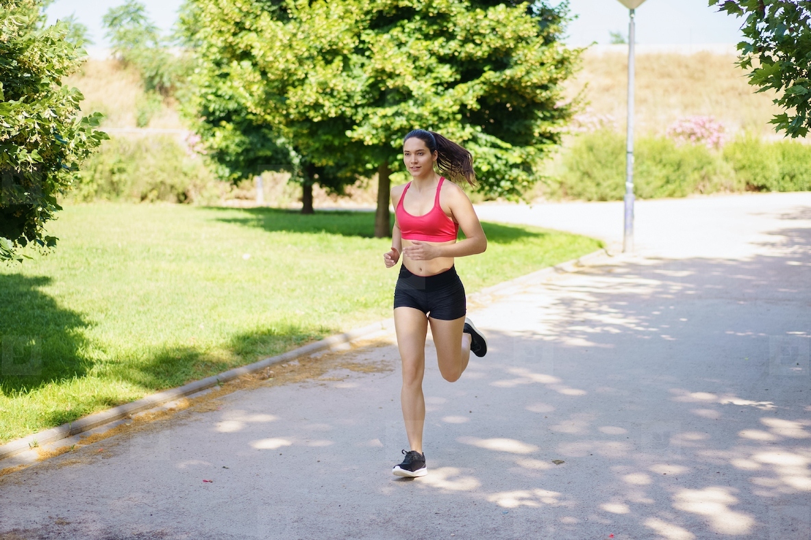 A young woman is jogging in the park enjoying nature exercising and embracing a healthy lifestyle