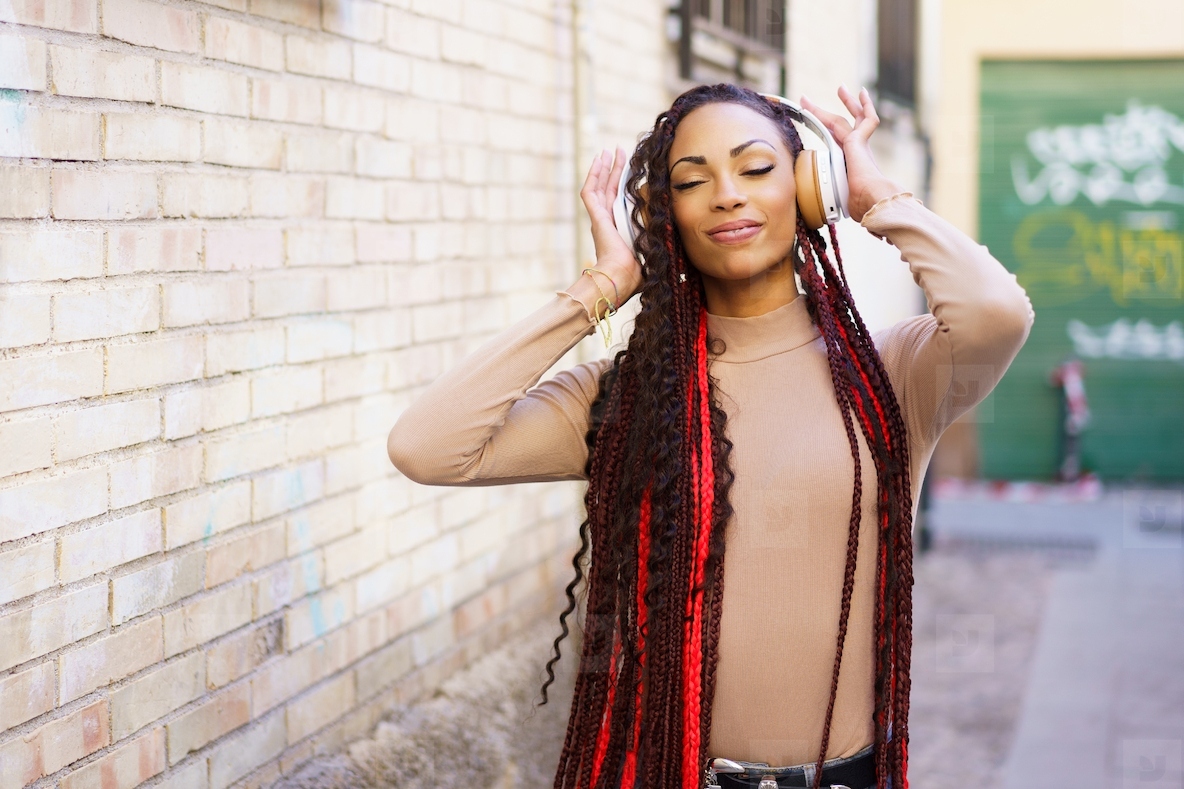 A young woman joyfully listens to music through headphones in a vibrant urban setting