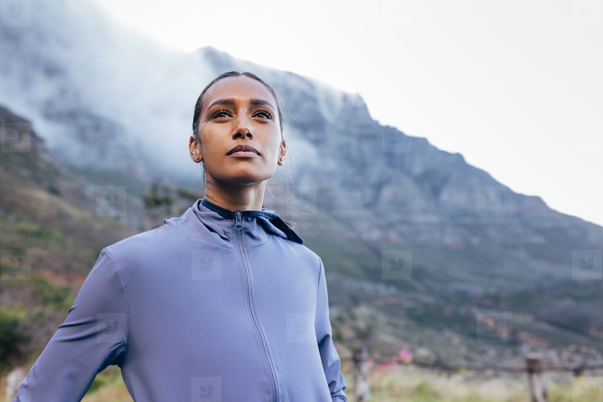 Portrait of a confident athlete standing outdoors against a mountain with clouds in the morning and looking into the distance