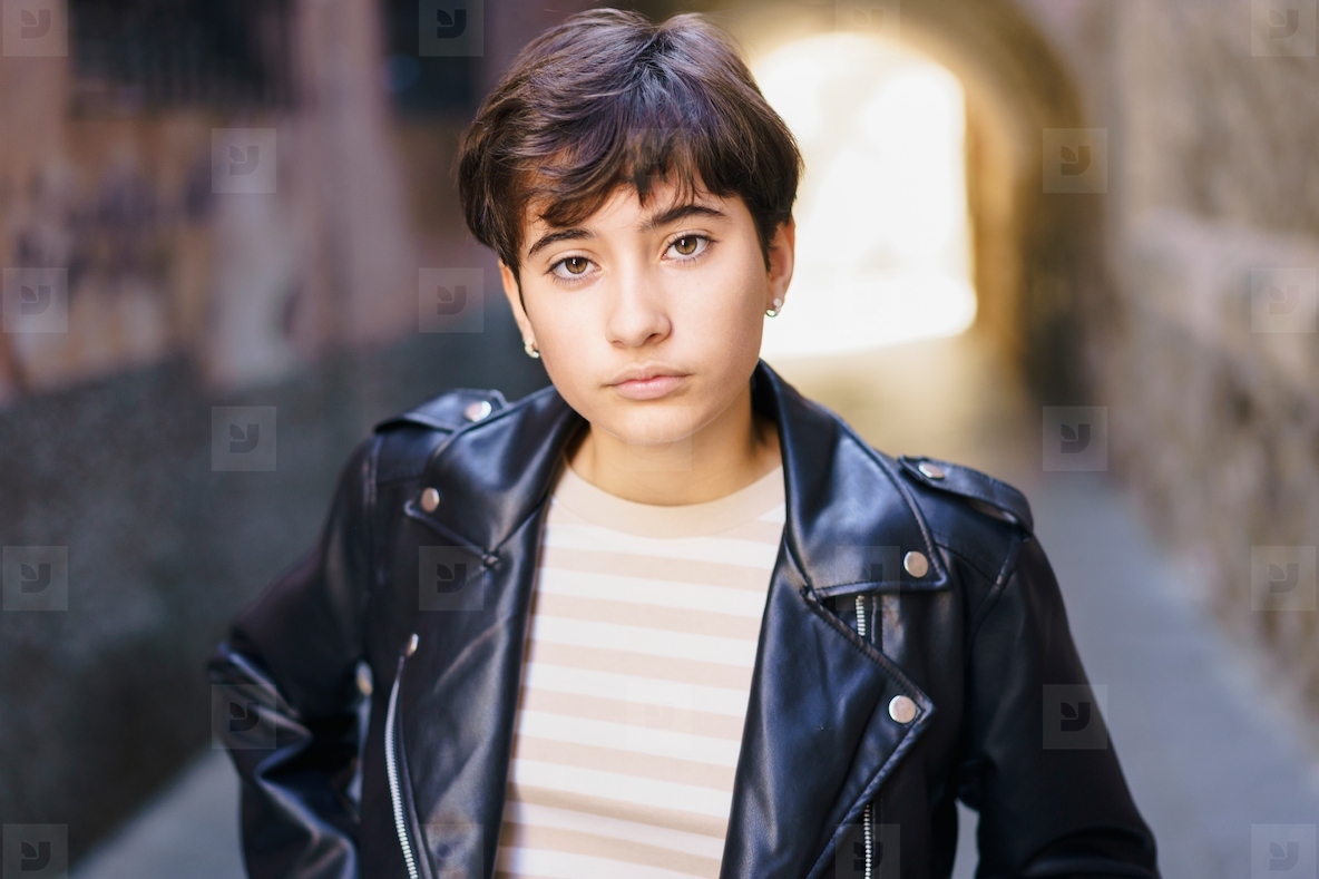 A Confident Young Woman Dressed in a Leather Jacket Poses Against an Urban Background