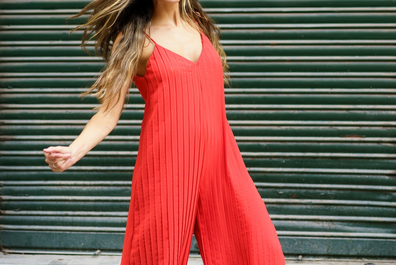 A vibrant red jumpsuit featuring a dynamic dance pose set against a lively green background