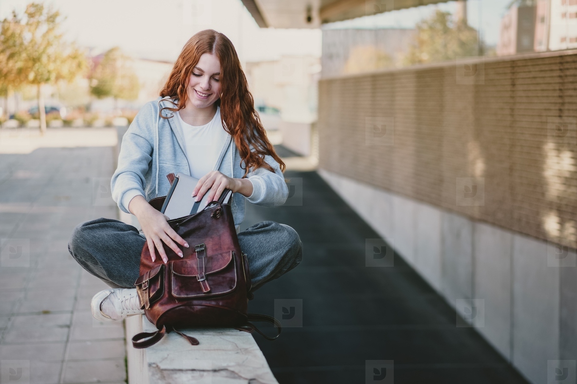 A Young Woman Sitting Outdoors with a Stylish Backpack in a Bustling Urban Setting
