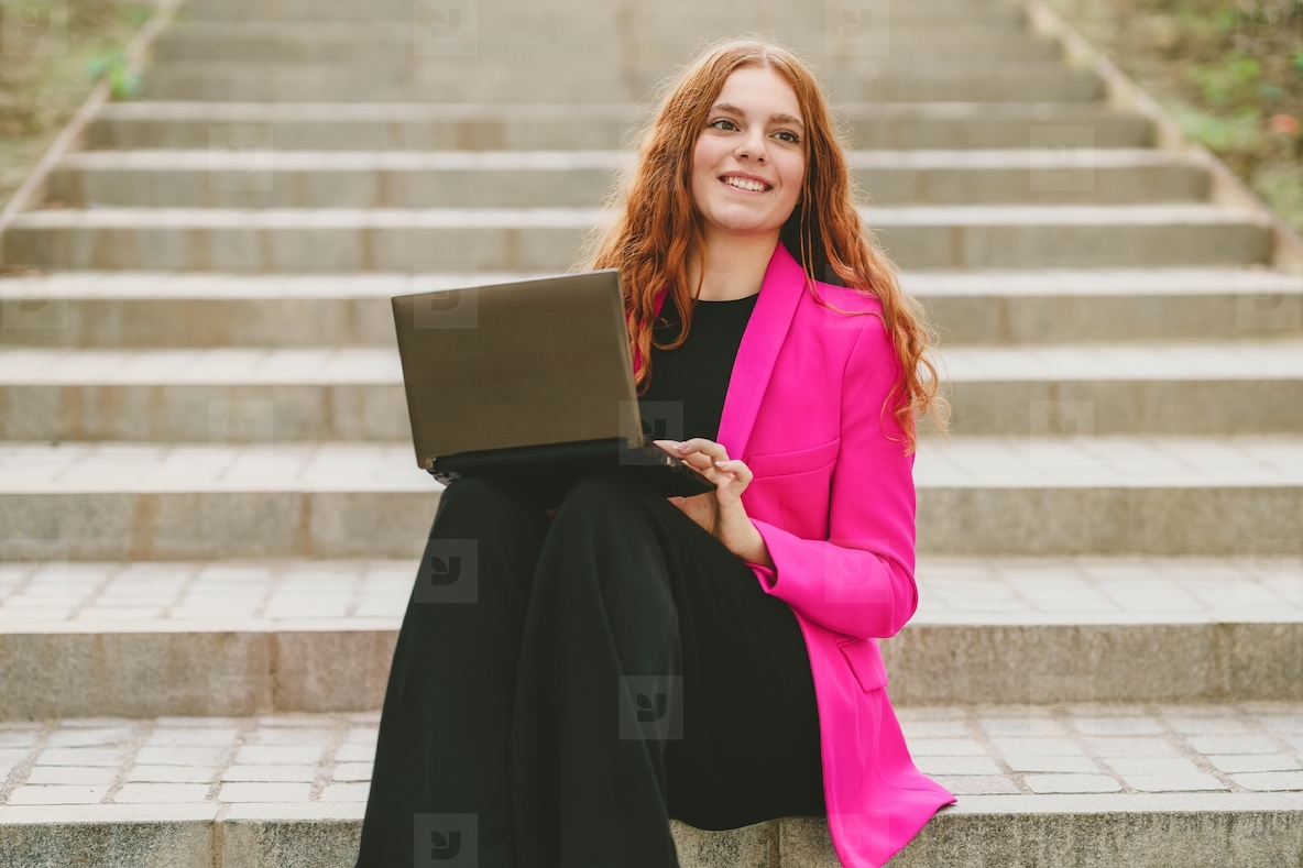 A Professional Young Woman Sitting on Outdoor Steps with a Laptop Engaging with Work