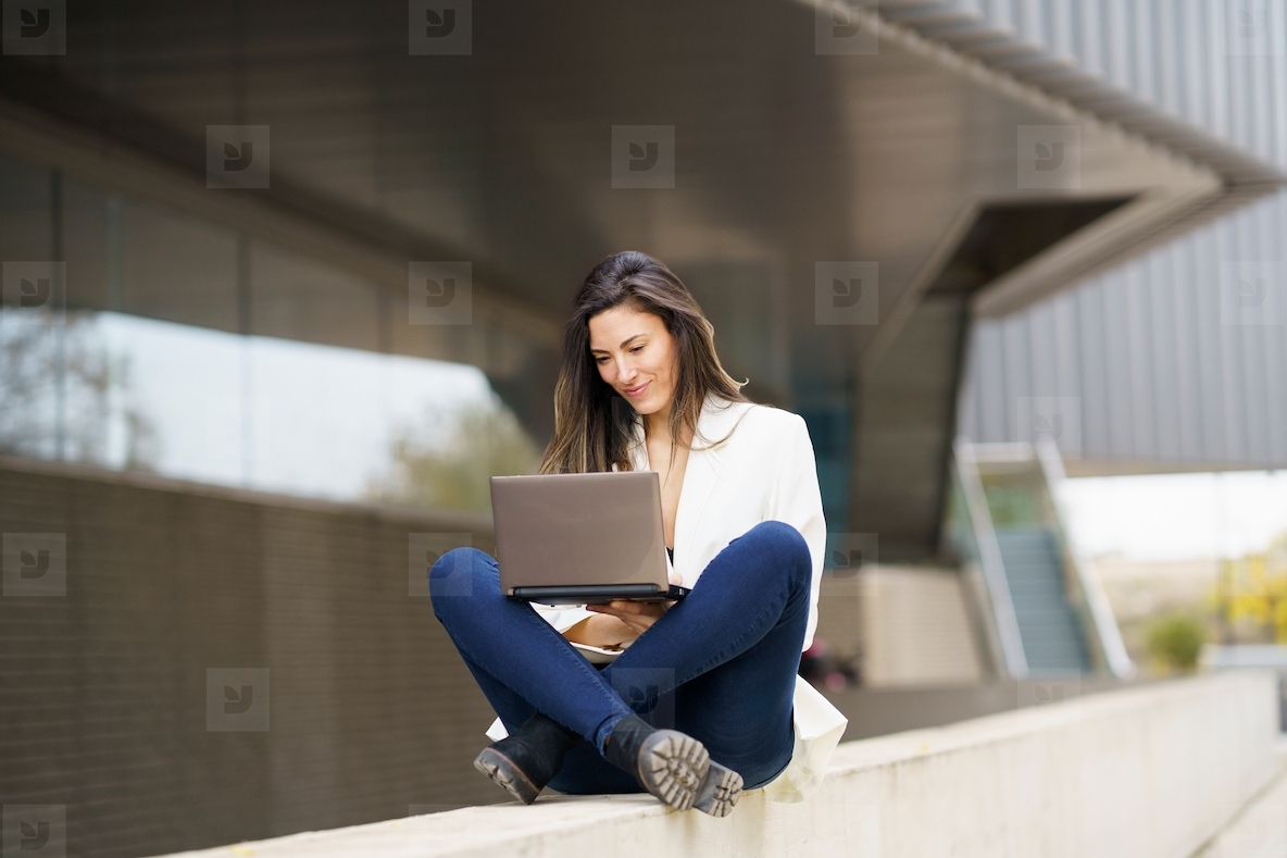 A Young Woman Concentrating While Working on a Laptop Outdoors in a Modern Urban Environment