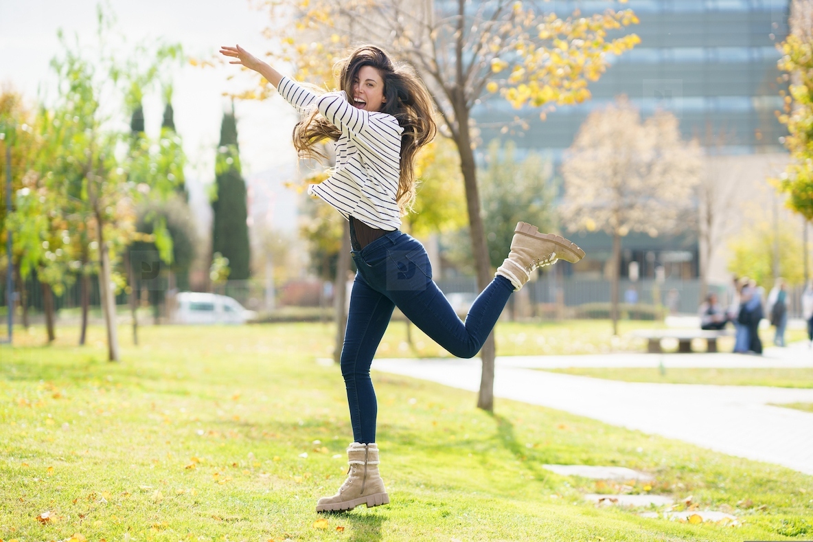 A Joyful Young Woman Dancing and Having Fun Outdoors in a Beautiful Autumn Park Scene