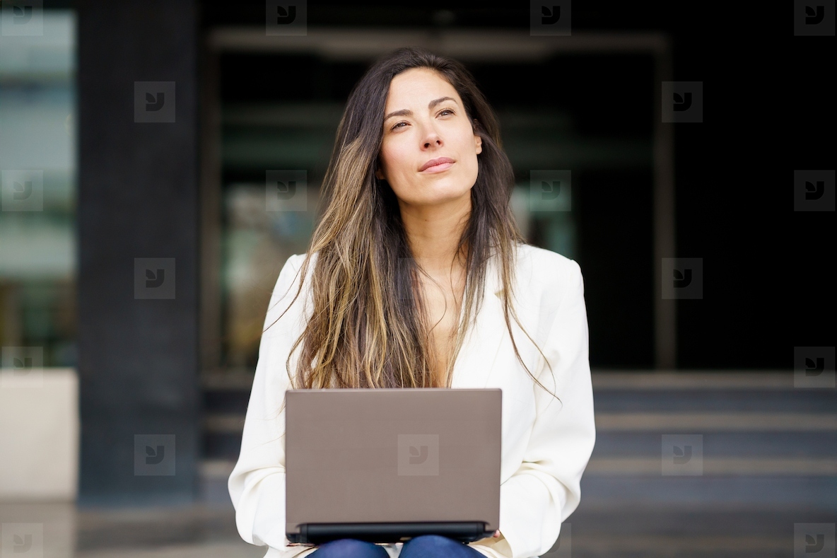 A thoughtful woman is diligently working on her laptop while savoring the stunning outdoors