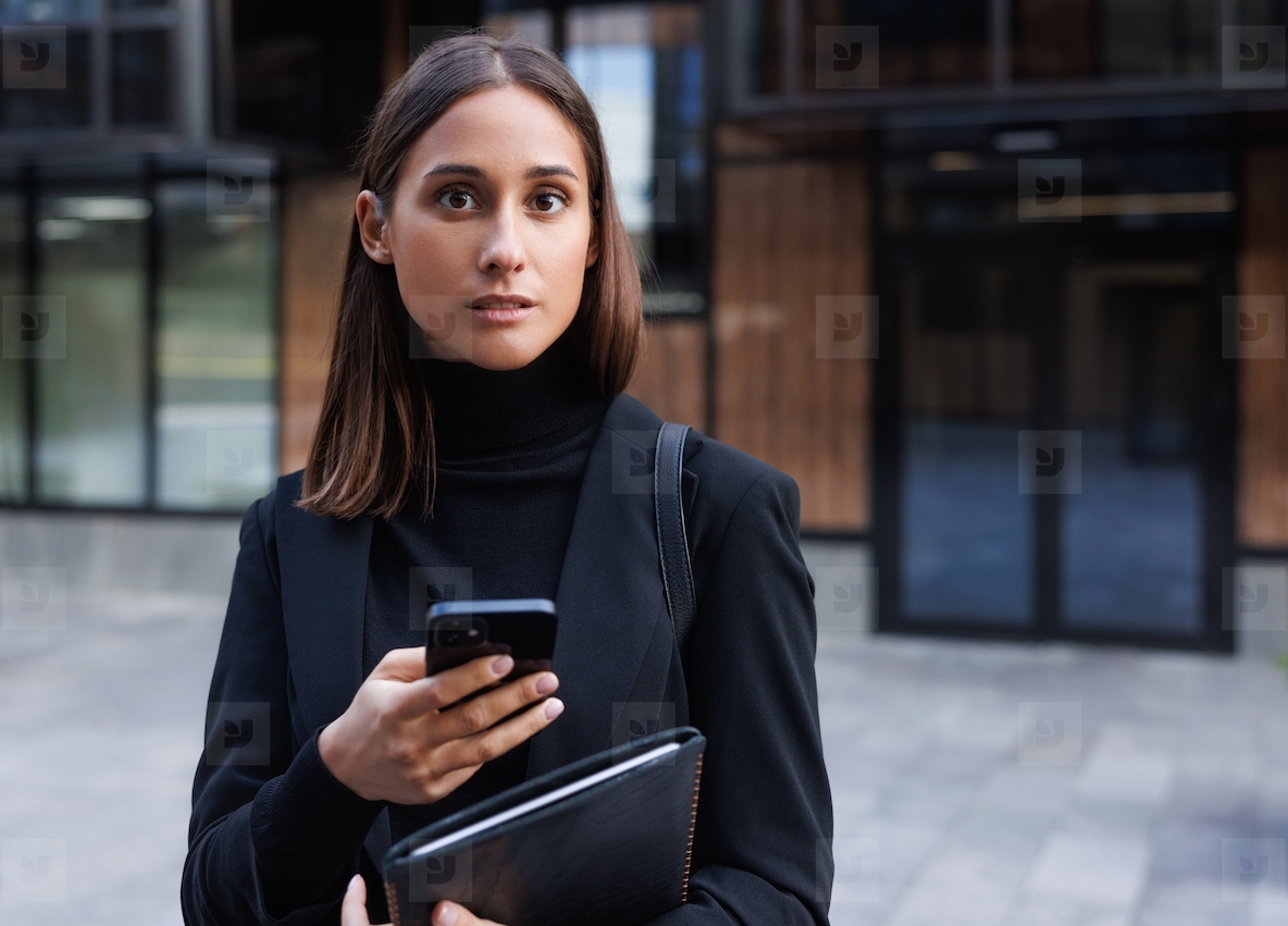 Portrait of a beautiful young businesswoman holding a smartphone and digital tablet and looking at a camera