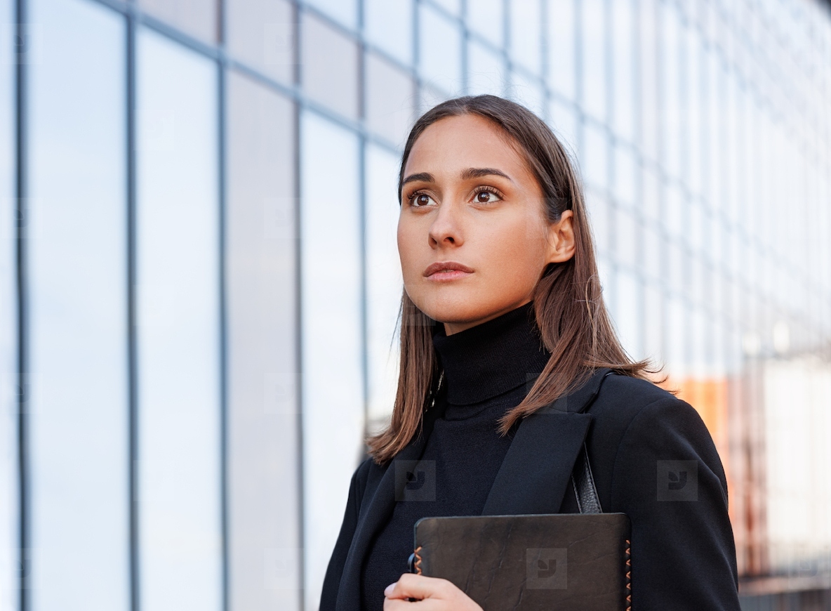 Portrait of a young female wearing black formal attire and looking into the distance while standing in front of a glass building