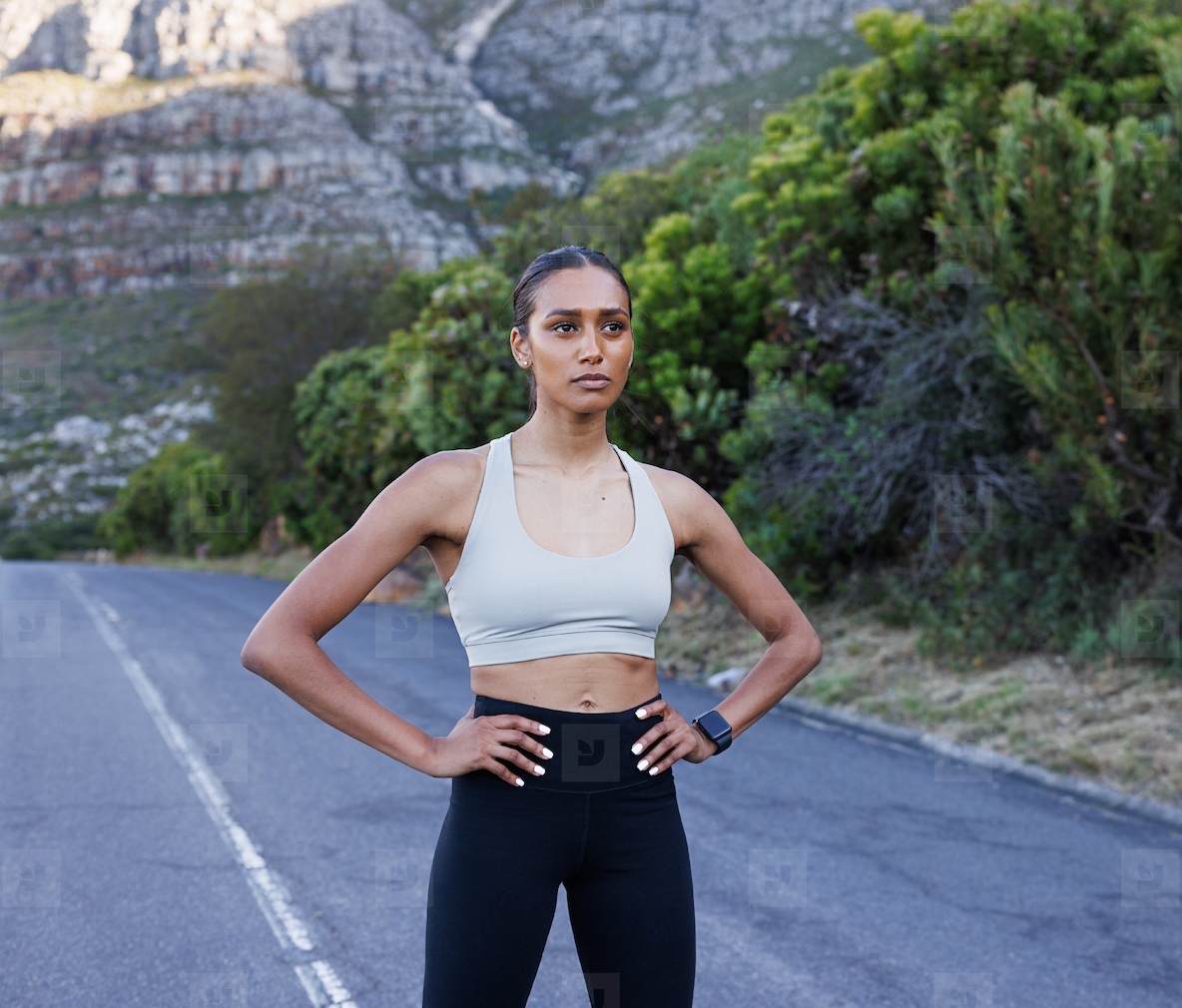 Slim confident woman in fitness attire with hands on her hips standing on an abandoned road