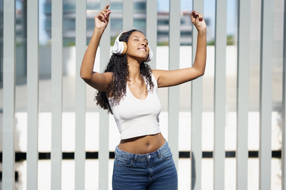 A Joyful Young Woman Enthusiastically Dancing with Headphones While Leaning Against a Wall