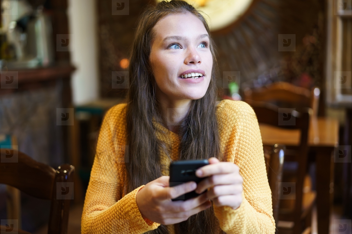 A Cheerful Young Woman is Engaged with Her Smartphone While Relaxing in a Cozy Cafe Setting
