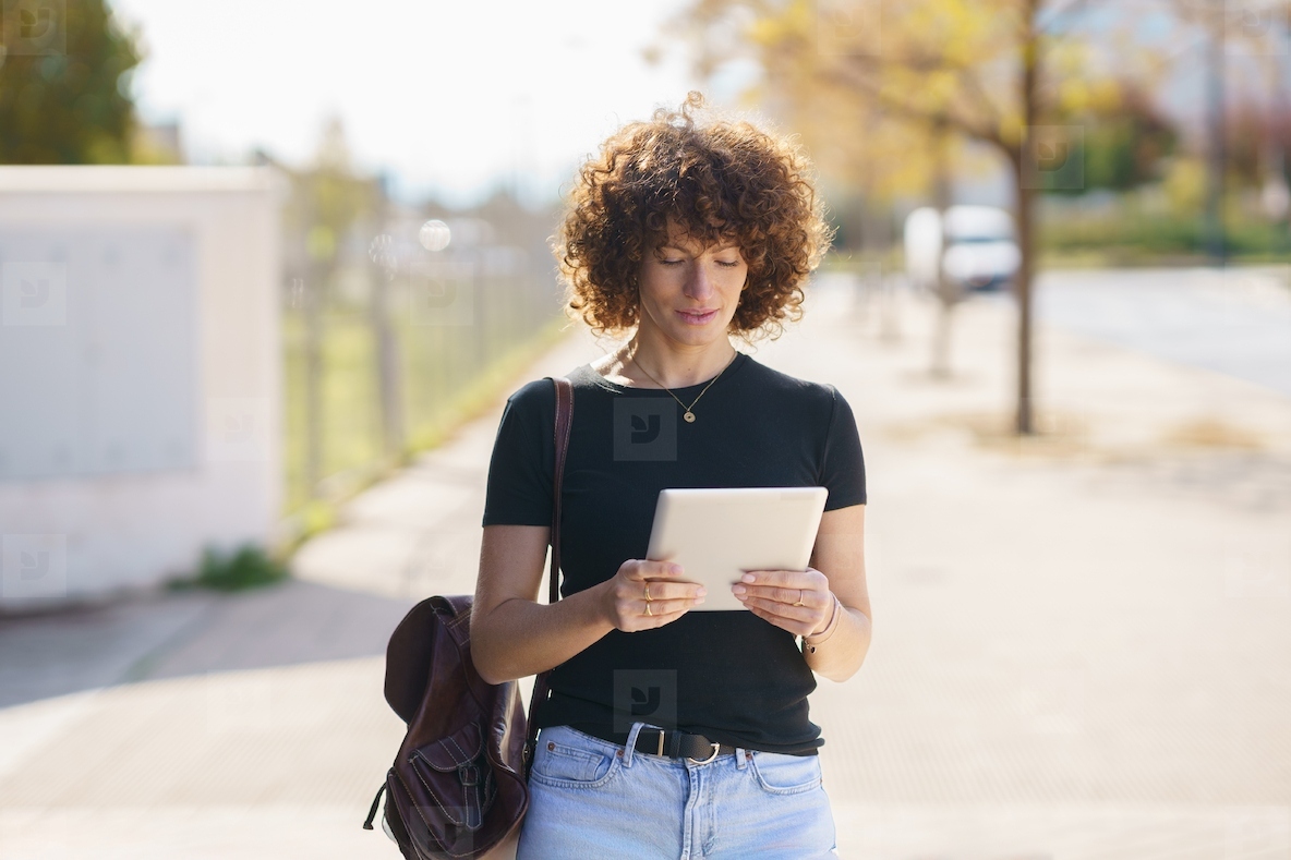 A young woman engaged in using a tablet while in an urban setting during daylight hours