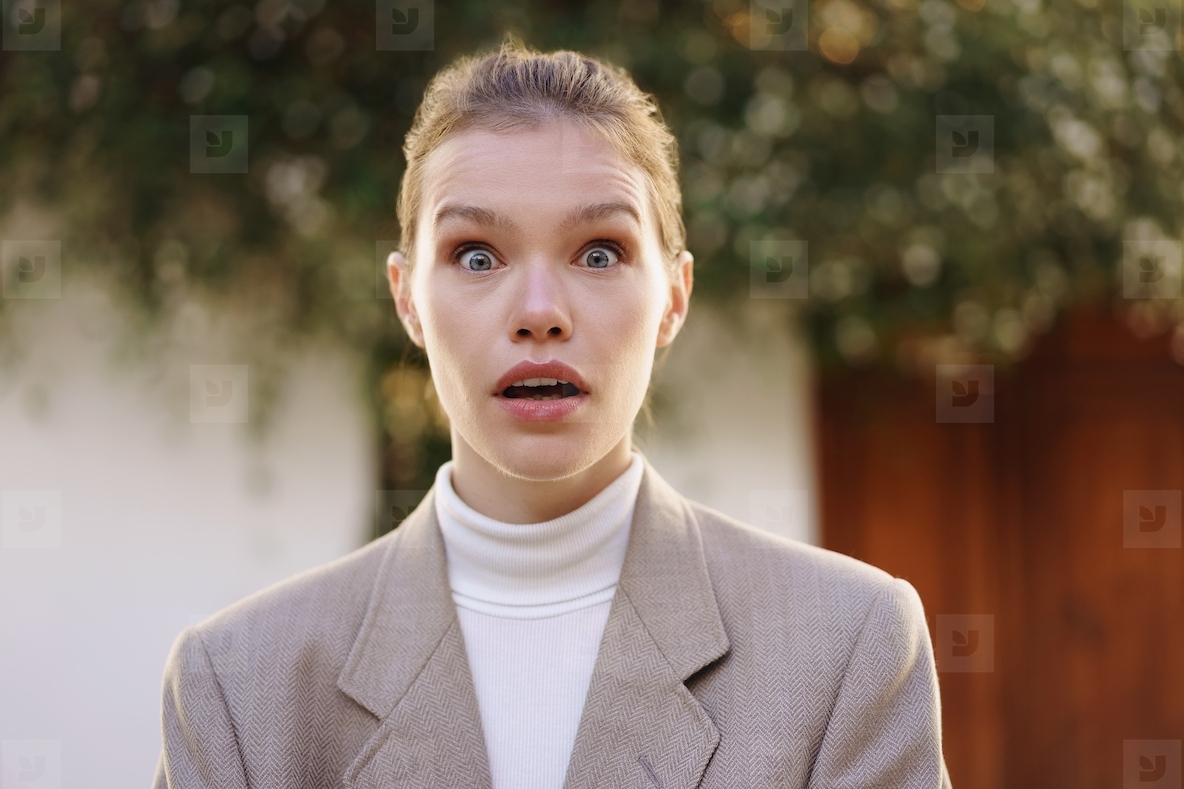 A surprised woman wearing a stylish outfit against a beautiful outdoor background scene