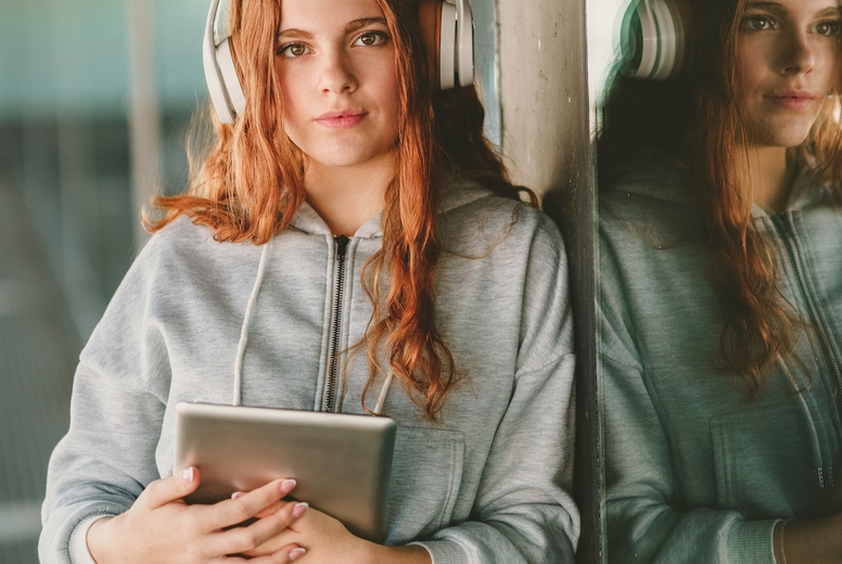 A Young Woman Wearing Headphones and Engaging with a Tablet While in a Vibrant Urban Setting