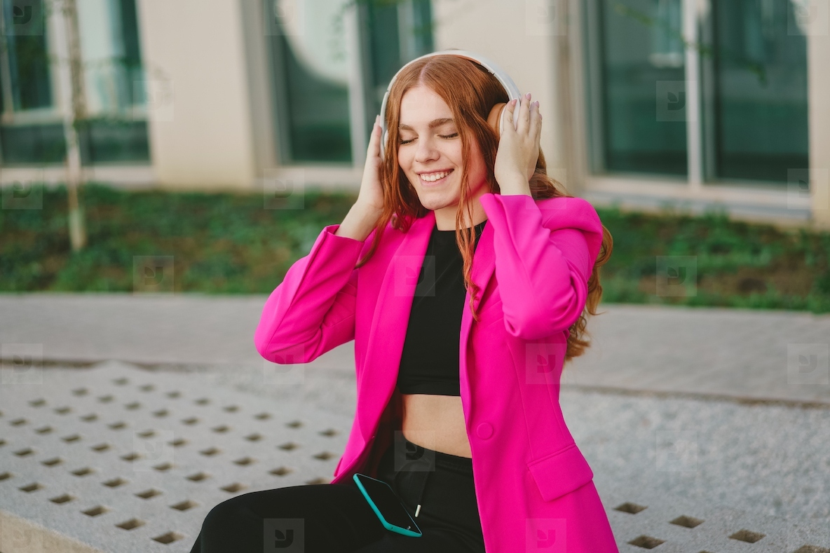 A young woman is enjoying her favorite music while dressed in a stylish pink blazer