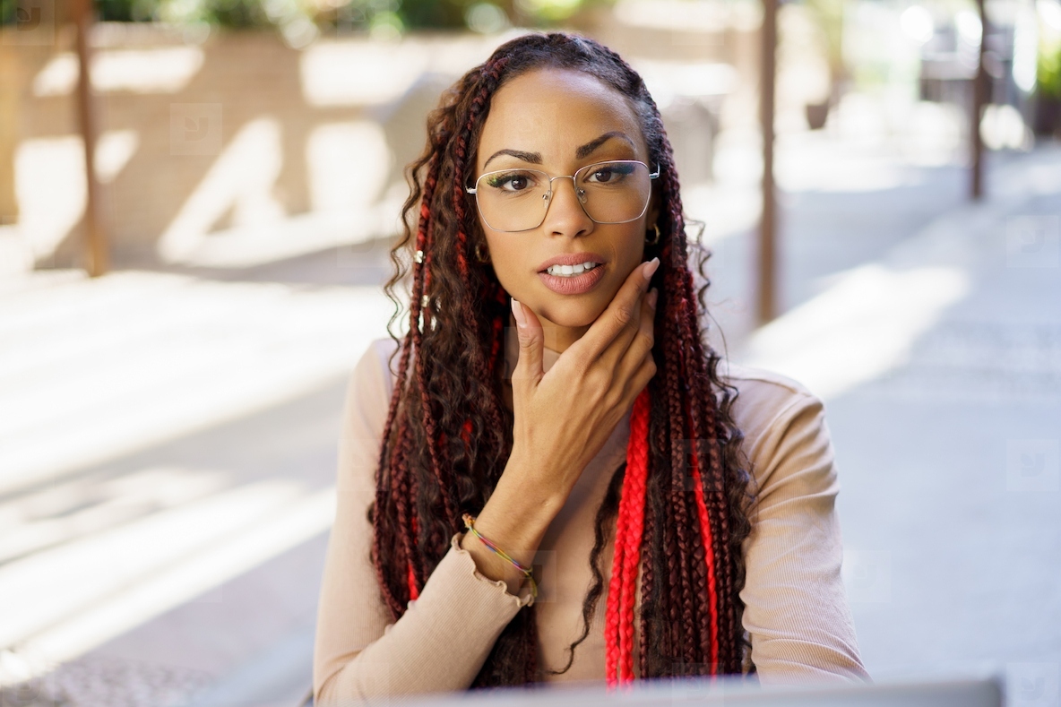 Confident woman in stylish glasses showcasing her braided hair at an outdoor workspace