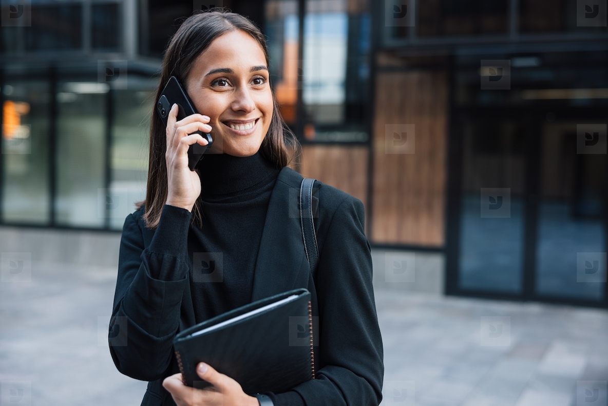 Smiling female wearing black formal wear with high collar  Businesswoman talking on her mobile phone while looking away