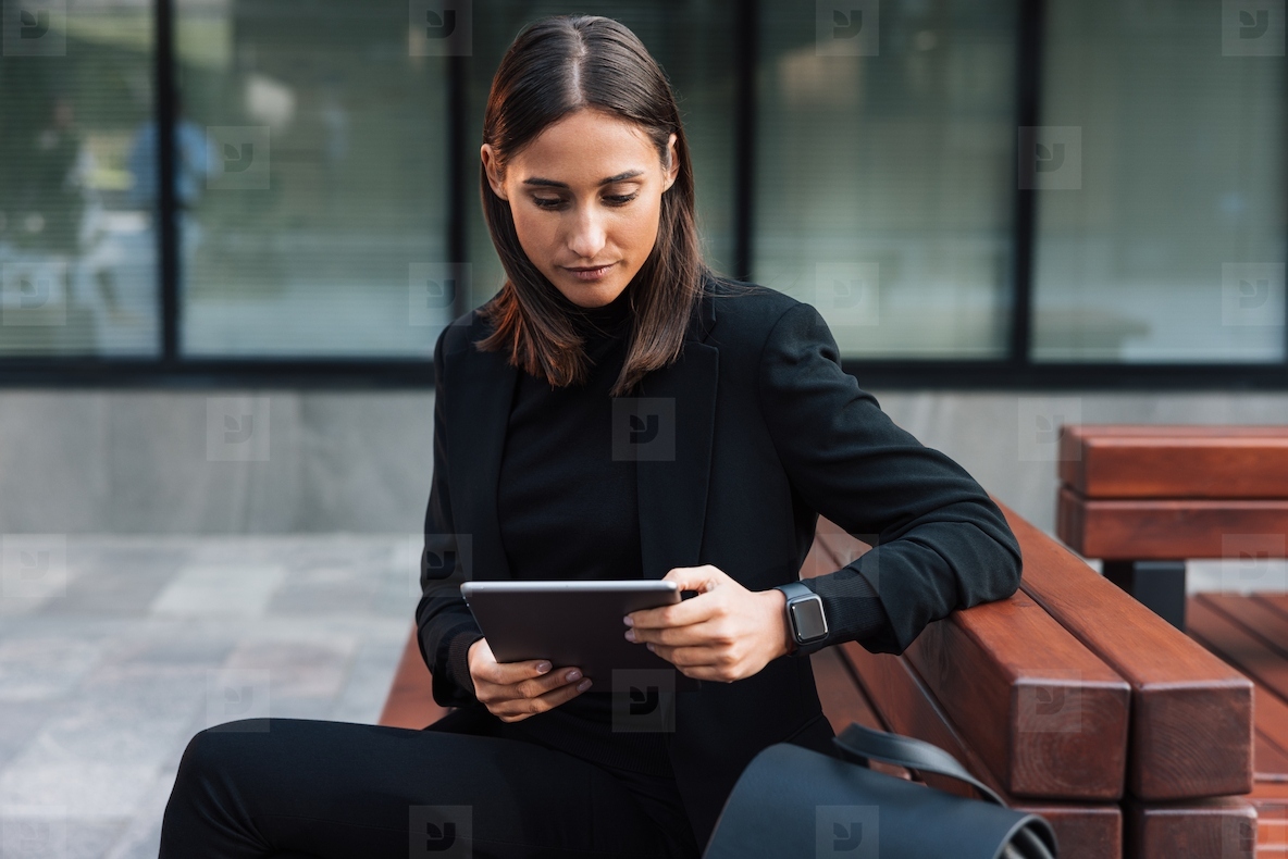 Young woman with digital tablet sitting outdoors wearing black stylish formal wear  Businesswoman reading from digital tablet