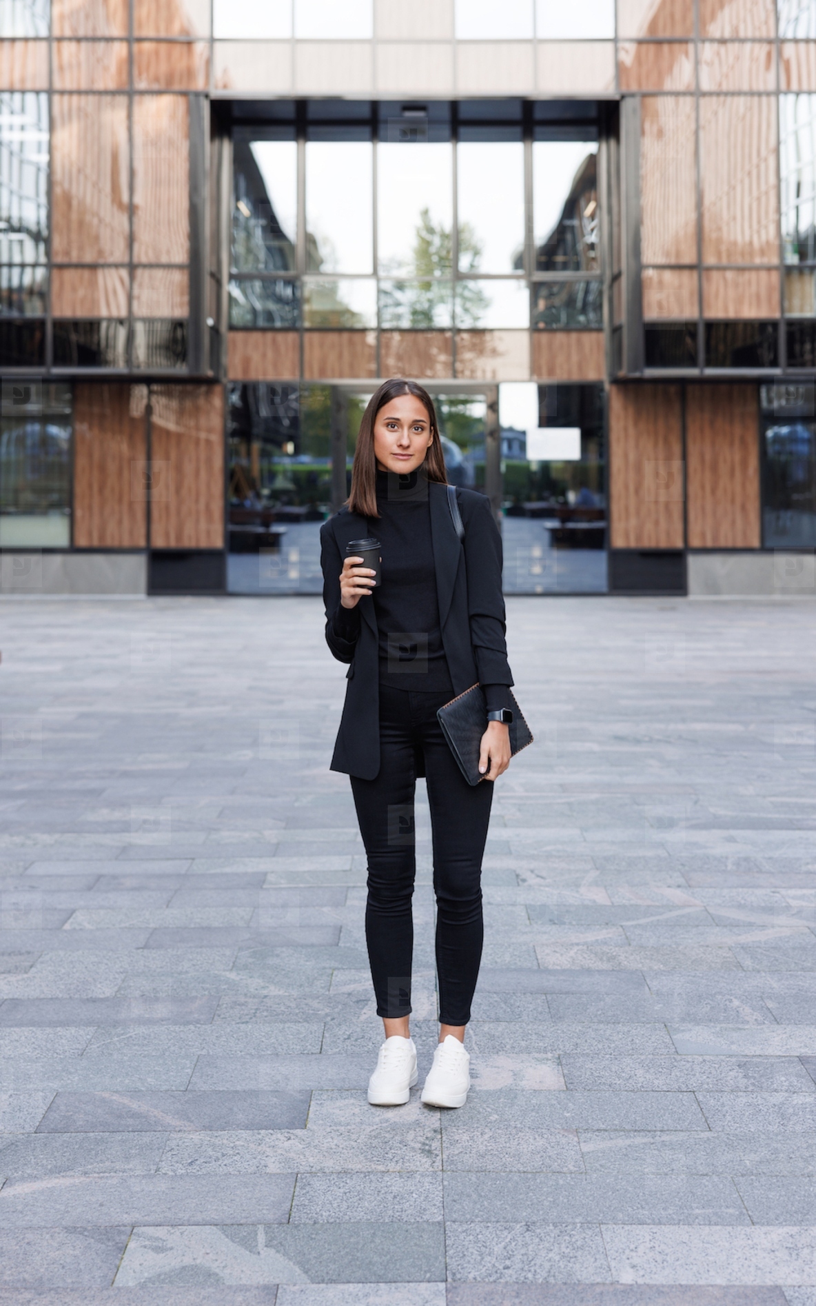 Full length of young female entrepreneur holding a digital tablet and coffee in front of an office building
