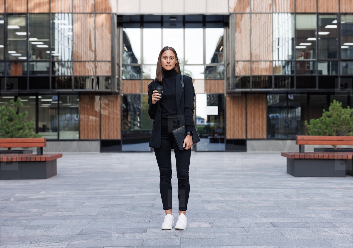 Full length of a female entrepreneur standing in office building outdoors  Business woman holding digital tablet and coffee cup outdoors