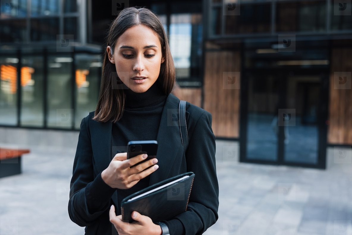 Portrait of a young woman entrepreneur using her mobile phone  Female wearing black stylish business attire holding digital tablet and smartphone