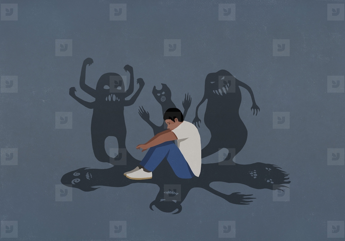 Shadows of monsters surrounding anxious teenage boy hugging knees