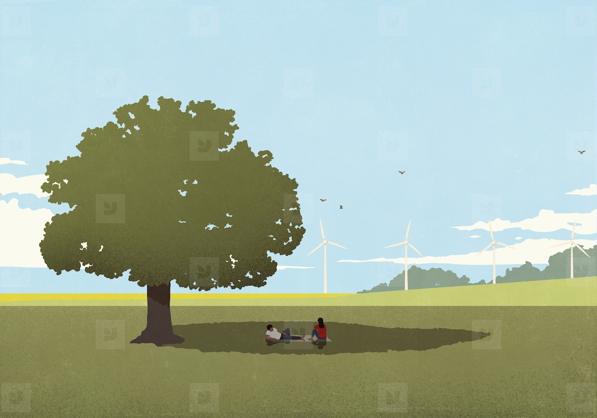 Couple relaxing on blanket in shade of tree in sunny field with wind turbines in the background