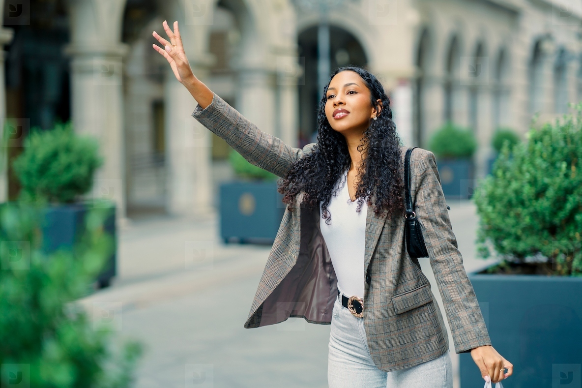 A Confident Young Woman Waving While Standing Outdoors in a Vibrant City Setting