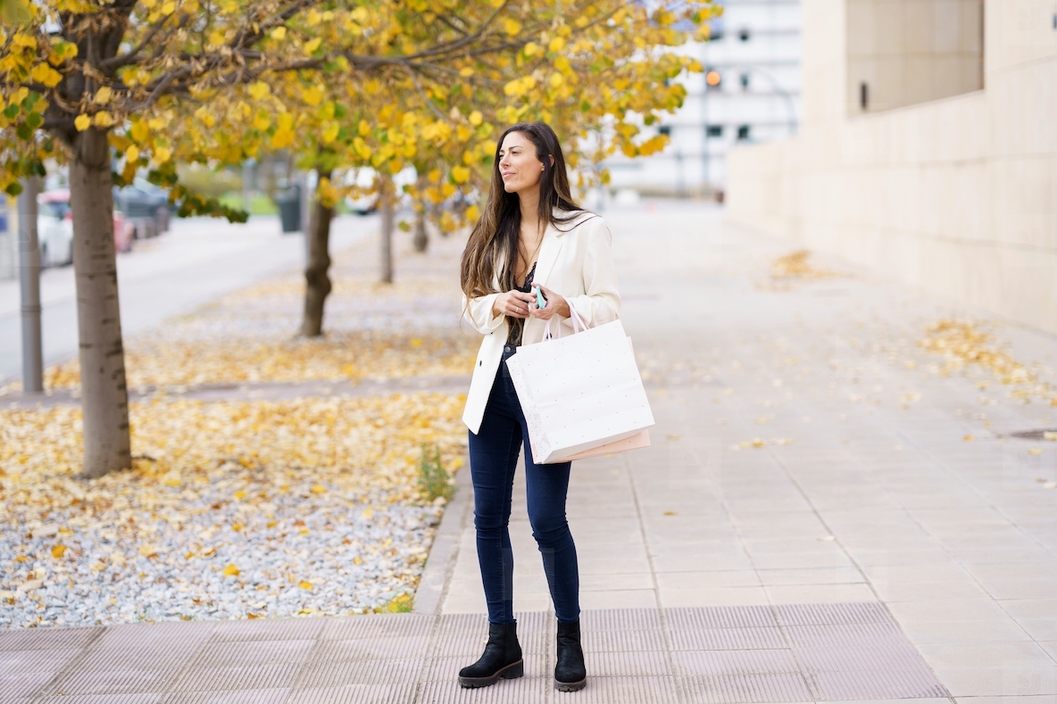 A young woman leisurely strolling down a beautiful autumn street  holding a shopping bag