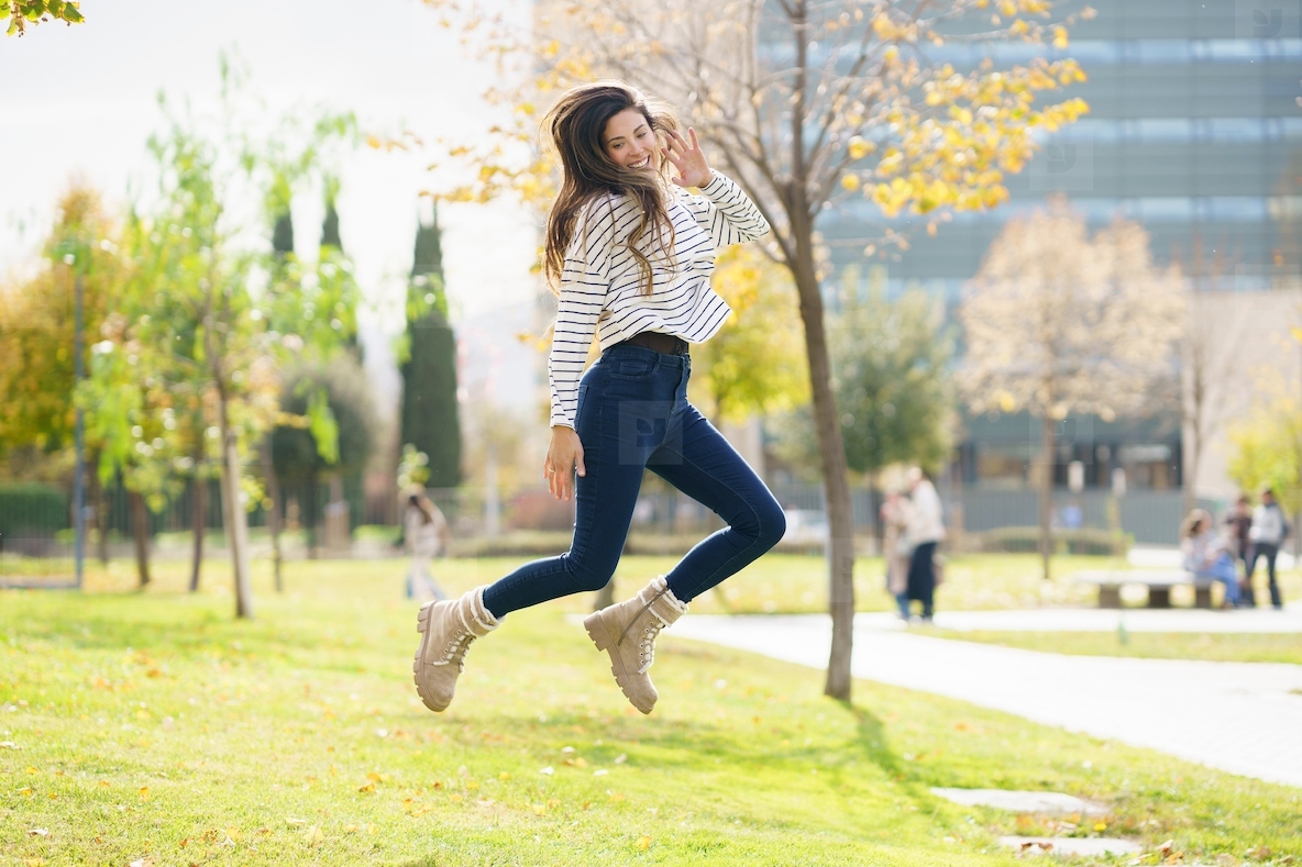 A joyful young woman is jumping in a beautiful sunny park filled with greenery and warmth