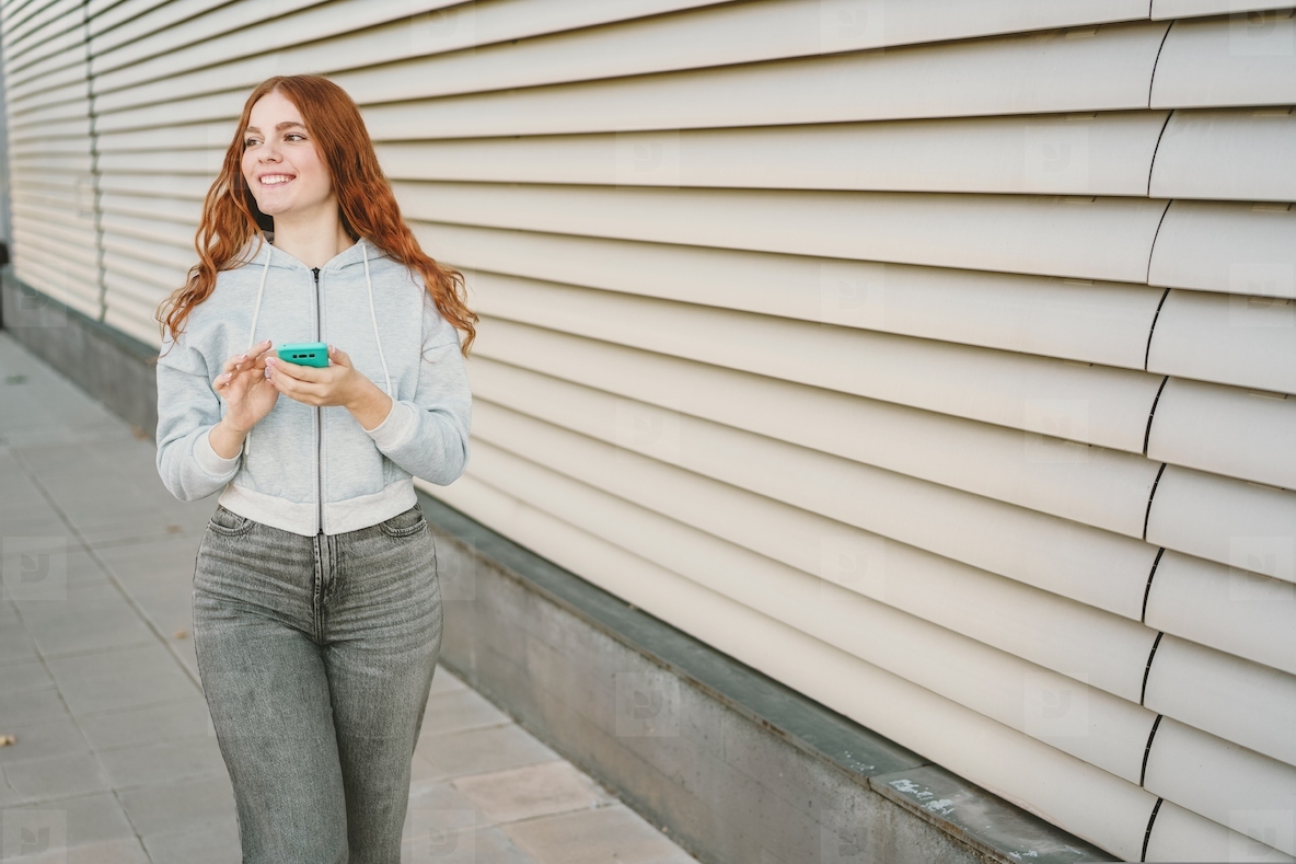 A young woman confidently holding her smartphone while standing against a modern wall
