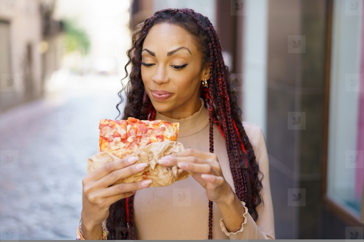 A Woman Happily Enjoying a Delicious Slice of Pizza in a Colorful and Charming Alleyway